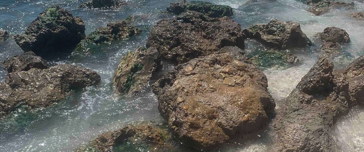 A rocky shoreline with clear turquoise water and waves crashing against the rocks.