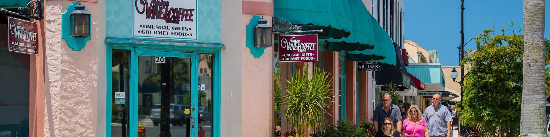 A street with storefronts, including a wine and coffee shop, and people walking on the sidewalk.