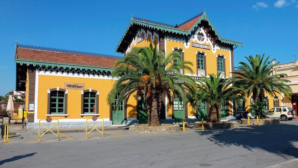 A yellow building with a green roof and palm trees in front.