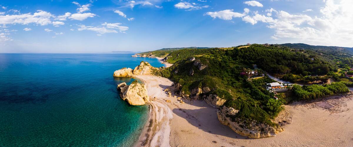 A coastal landscape with a clear blue sea, a sandy beach, and rocky cliffs.