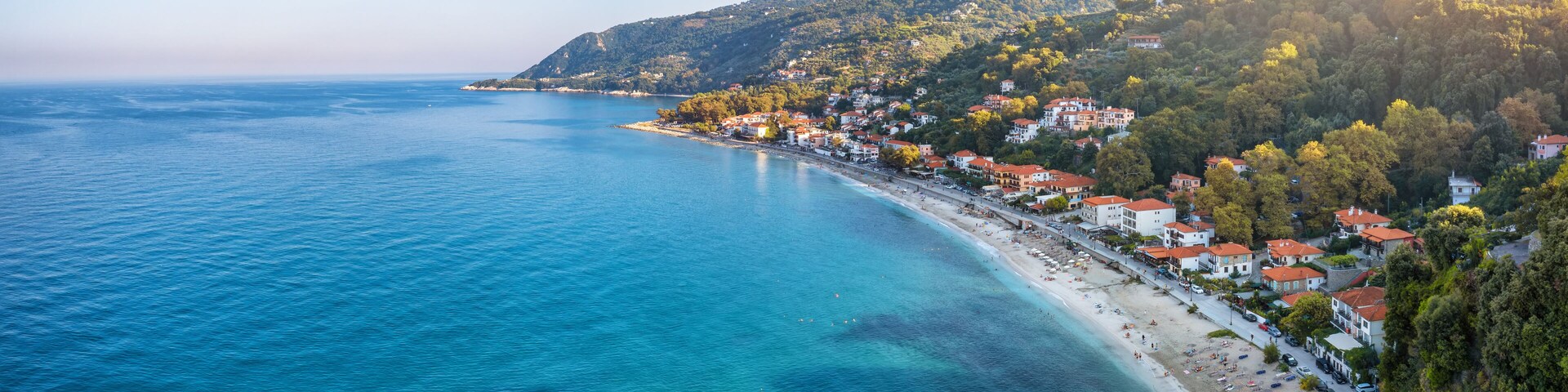 Un pueblo costero con playa, casas y un paisaje montañoso de fondo.