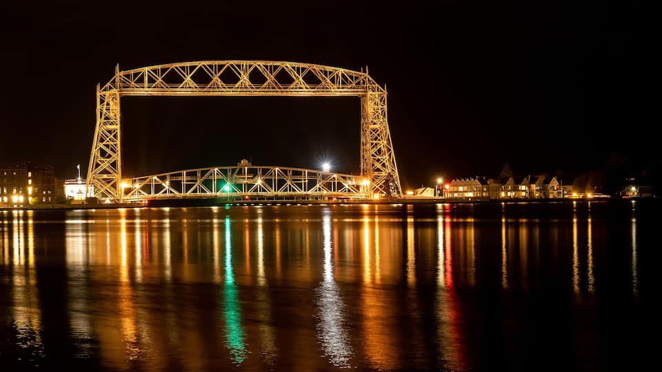 A large illuminated bridge at night with its reflection on the water.