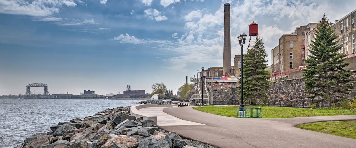 A riverside walkway with a stone wall, a metal staircase, and a red water tower.