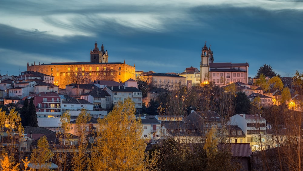 A historic cityscape with a prominent castle and church, surrounded by residential buildings and autumn foliage.