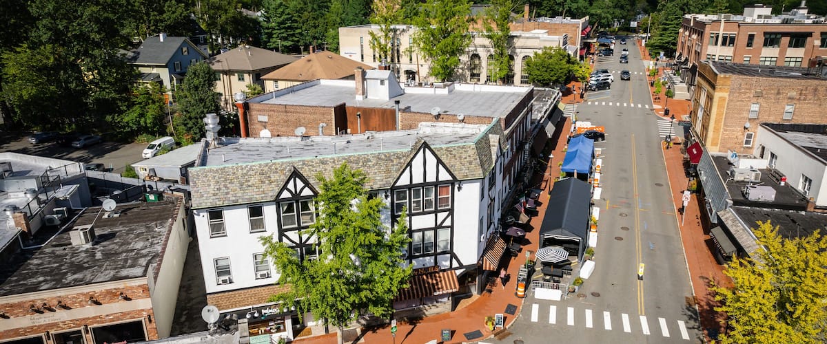 A town square with historic buildings, a crosswalk, and a street lined with parked cars.