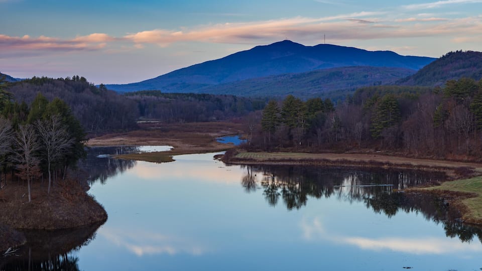 A calm lake surrounded by forested hills and a mountain in the background.