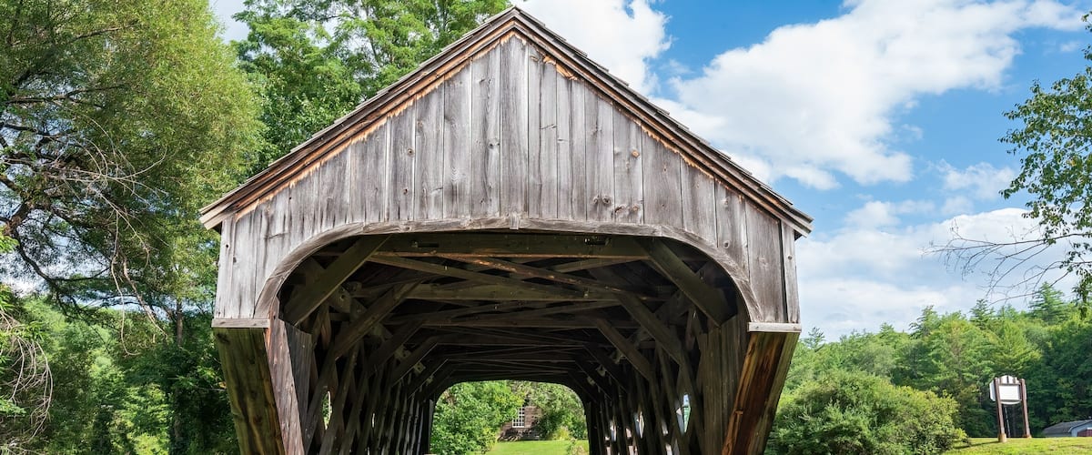 East end of the Baltimore covered bridge is an old wooden bridge located in Springfield Vermont with dark weathered wood located next to the Eureka one-room schoolhouse. Summer day in full sun.