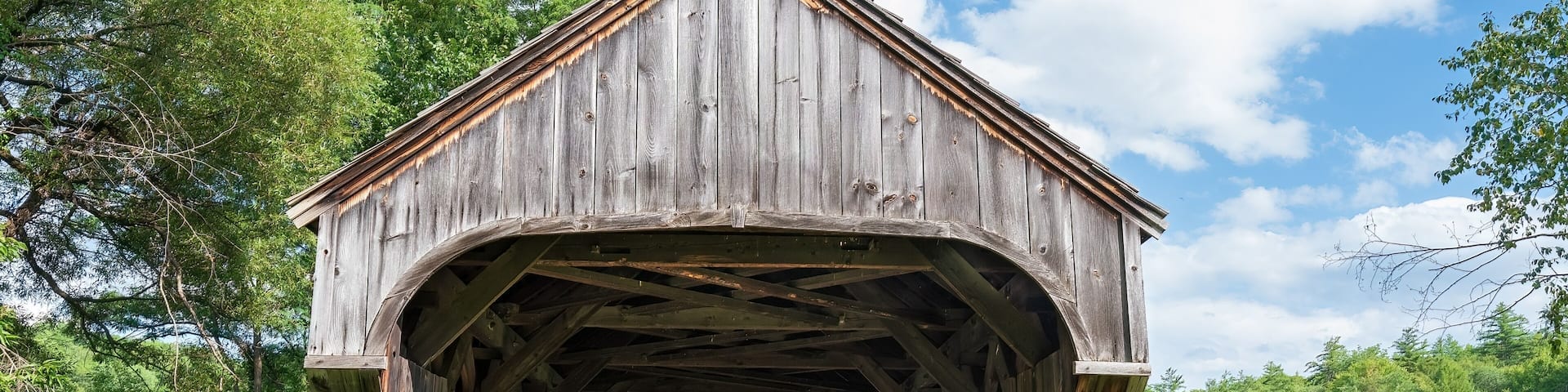 East end of the Baltimore covered bridge is an old wooden bridge located in Springfield Vermont with dark weathered wood located next to the Eureka one-room schoolhouse. Summer day in full sun.