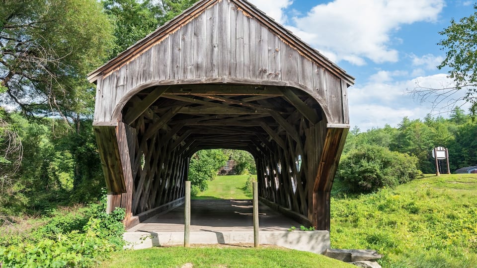 A wooden covered bridge in a lush green landscape.