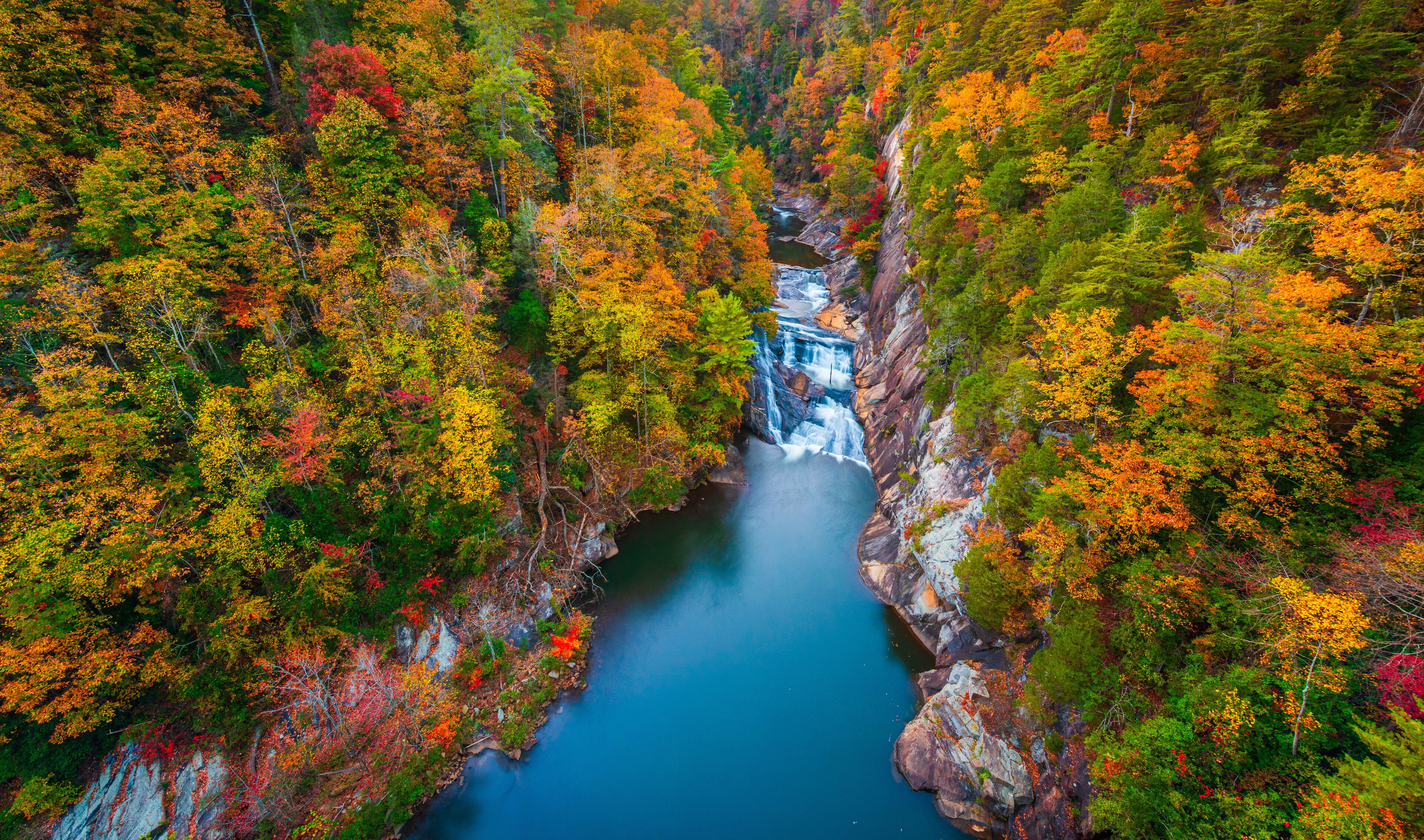 A canyon with a waterfall surrounded by autumn-colored trees.
