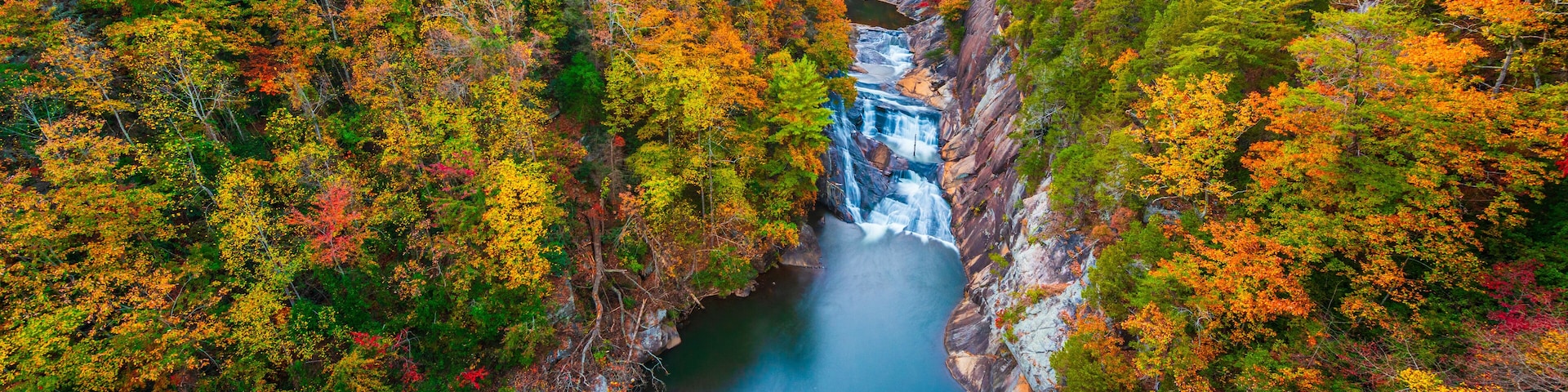 Un cañón con una cascada rodeado de árboles de colores otoñales.