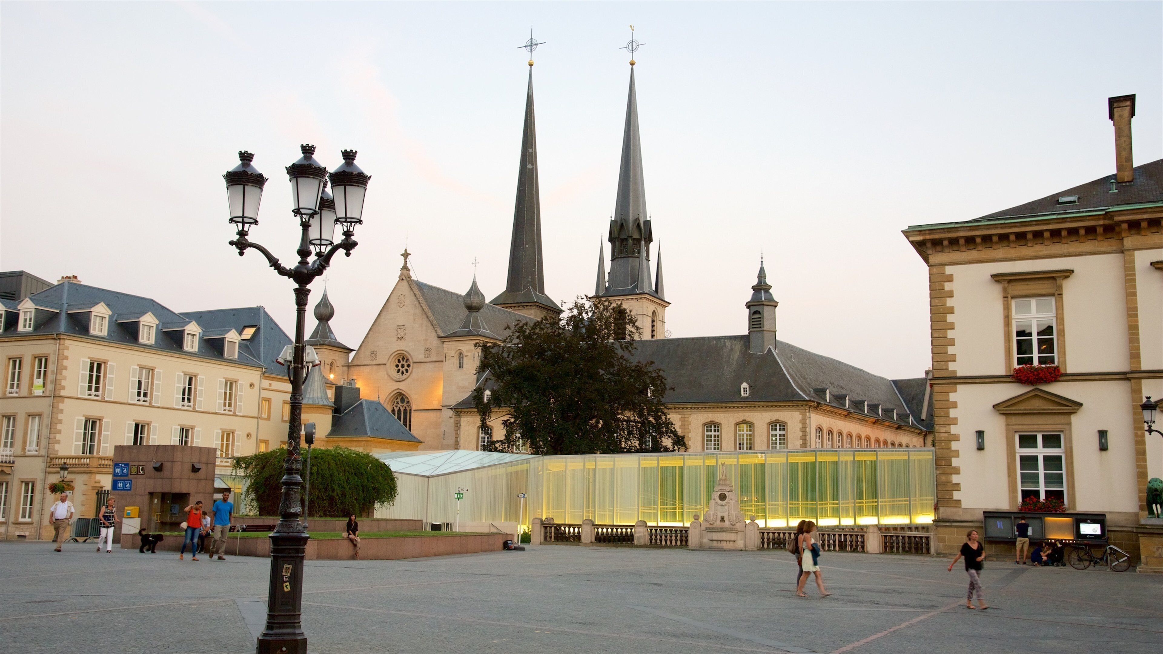 A historic square with a church featuring two tall spires, a street lamp, and a modern glass structure.