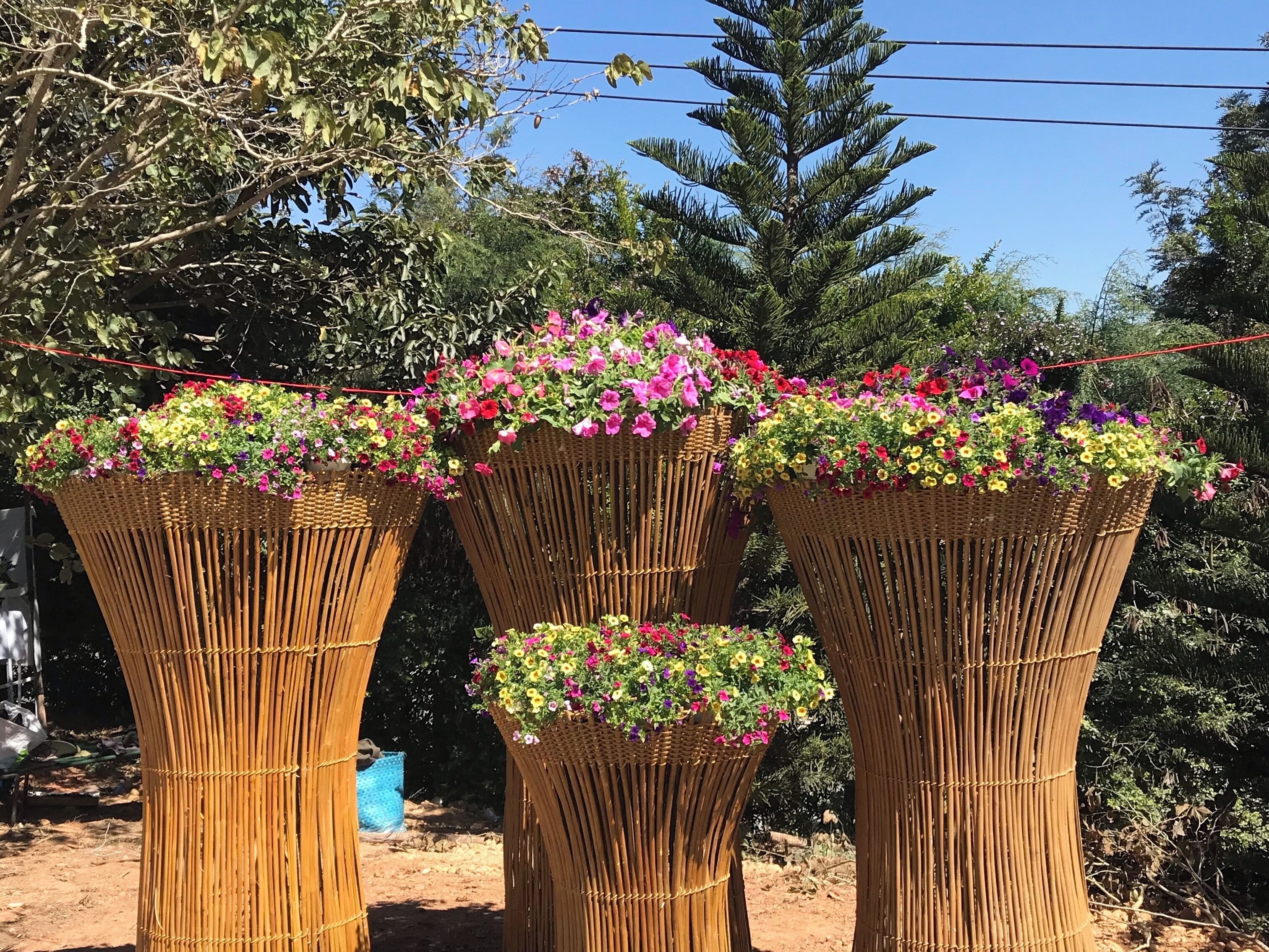 Three tall, cylindrical bamboo baskets filled with colorful flowers.