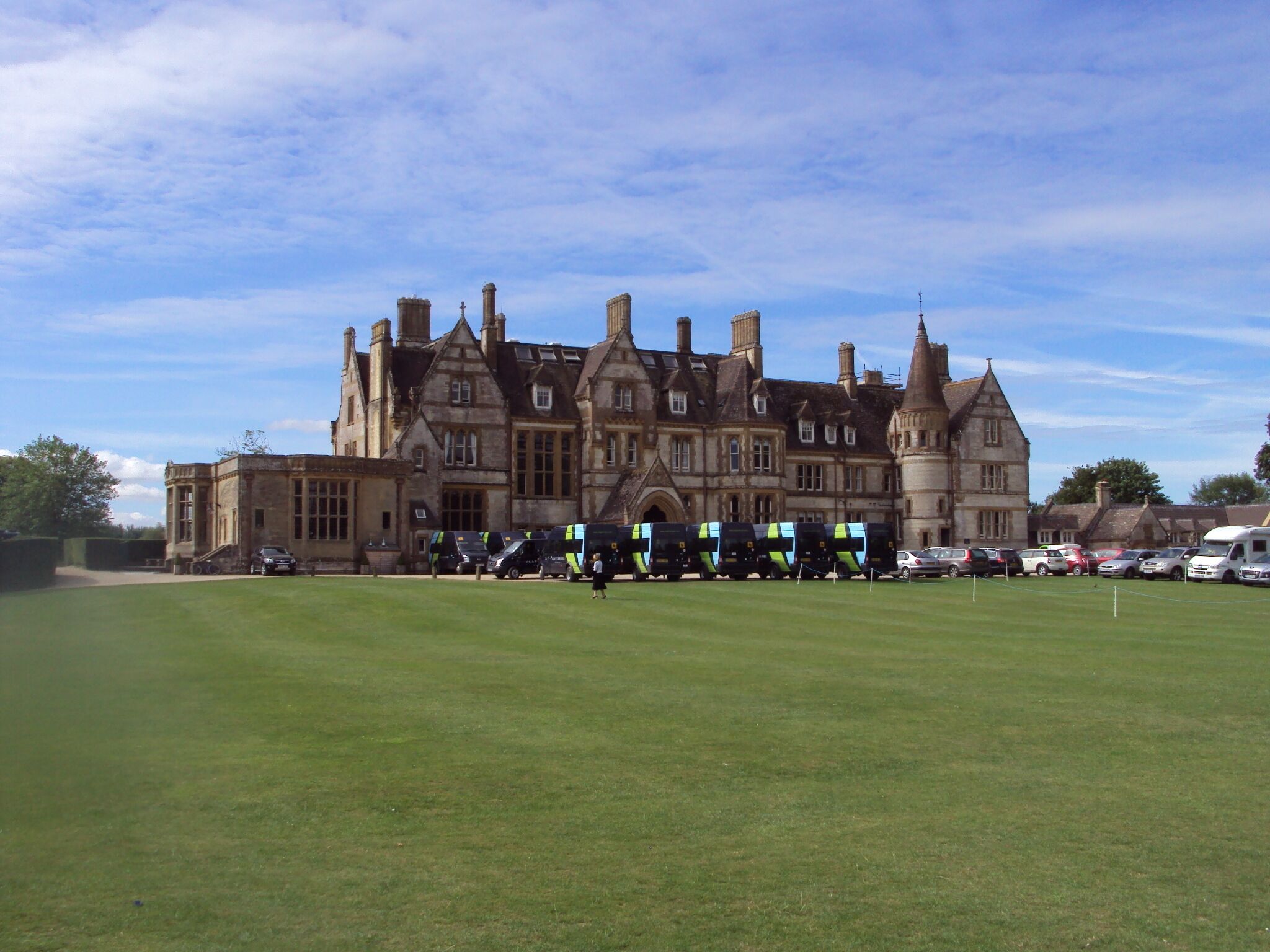 A large, historic building with multiple chimneys and a well-maintained lawn in front.