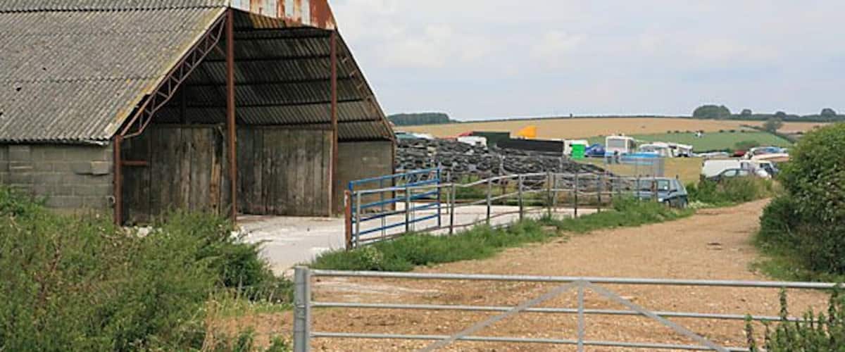 A rustic barn with a metal roof, a metal gate, and a dirt path leading to it.