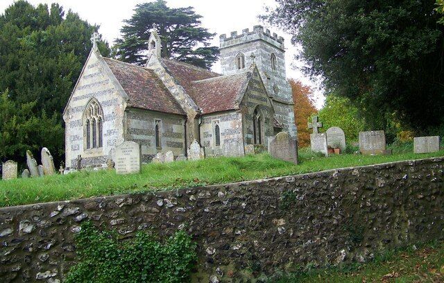 A stone church with a steep roof and a bell tower, surrounded by headstones and trees.