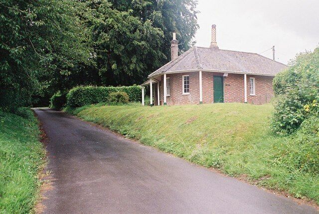 A rural road leading to a brick house with a green door, surrounded by greenery.