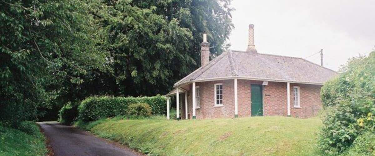 A rural road leading to a brick house with a green door, surrounded by greenery.