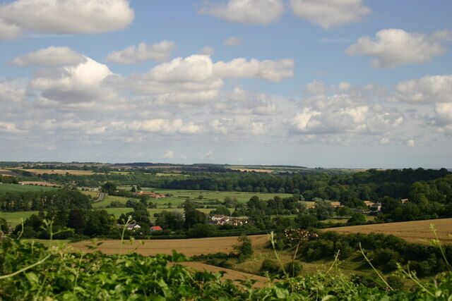 A rural landscape with rolling hills, scattered houses, and a clear sky with clouds.