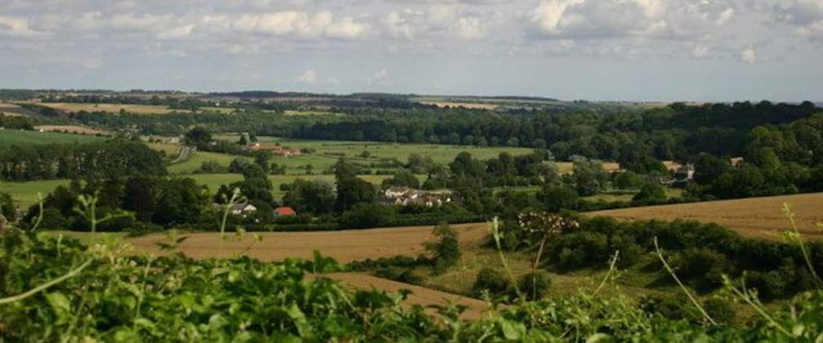 A rural landscape with rolling hills, scattered houses, and a clear sky with clouds.