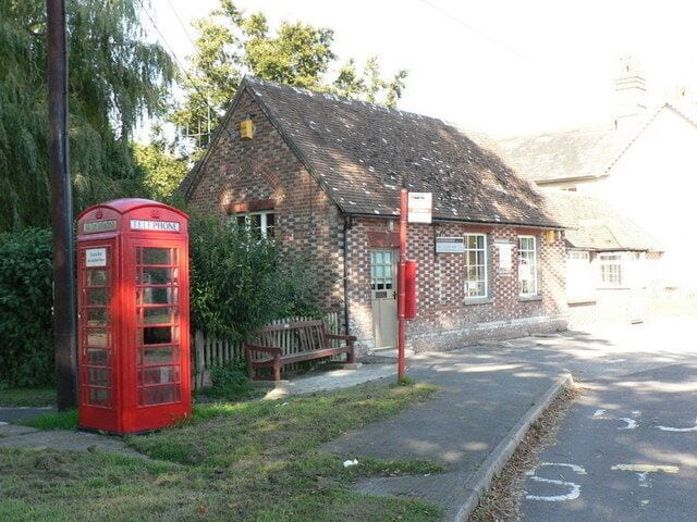 Una cabina telefónica roja, un edificio de ladrillo y una carretera con señal de límite de velocidad.