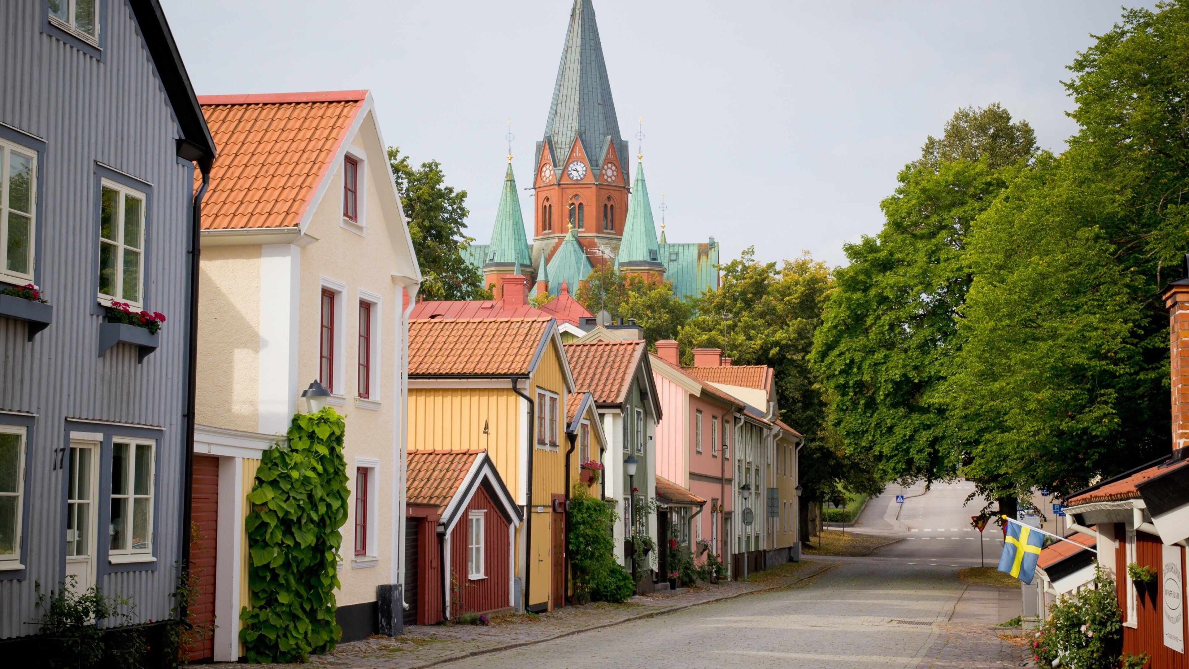 A street lined with colorful houses, a church with a tall spire, and a Swedish flag.
