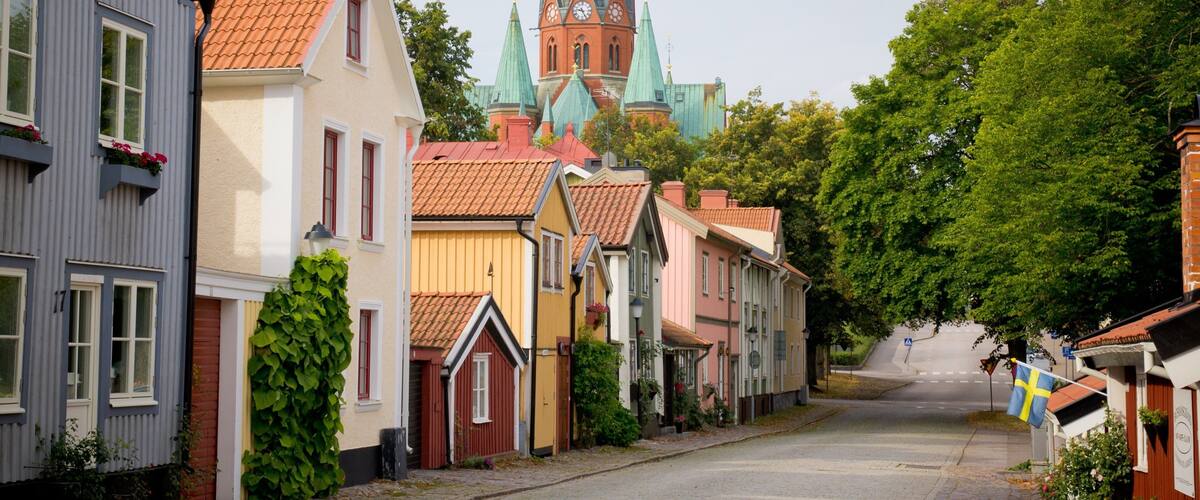 A street lined with colorful houses, a church with a tall spire, and a Swedish flag.