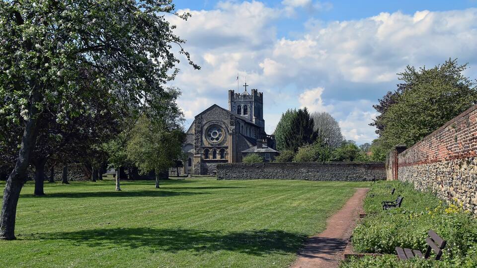 A church with a clock tower, surrounded by a well-maintained lawn and a brick wall.