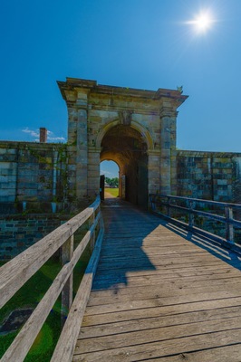 A stone archway leading through a wooden bridge with a metal railing.