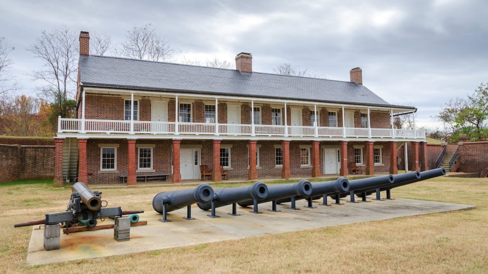 A historic brick building with a balcony, a row of cannons, and a cannon on display.