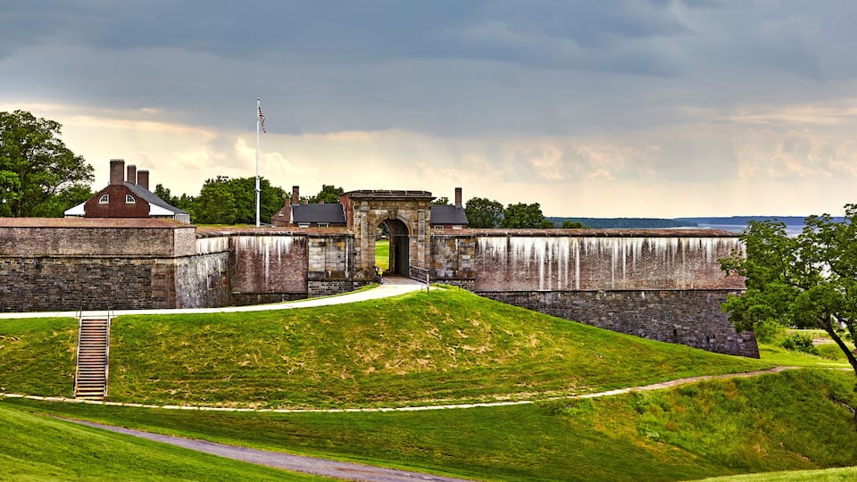A historic fort with a large gate, a flagpole, and a grassy hill.