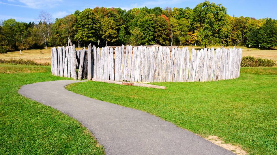 A winding path leading to a wooden fence in a park with green grass and trees in the background.