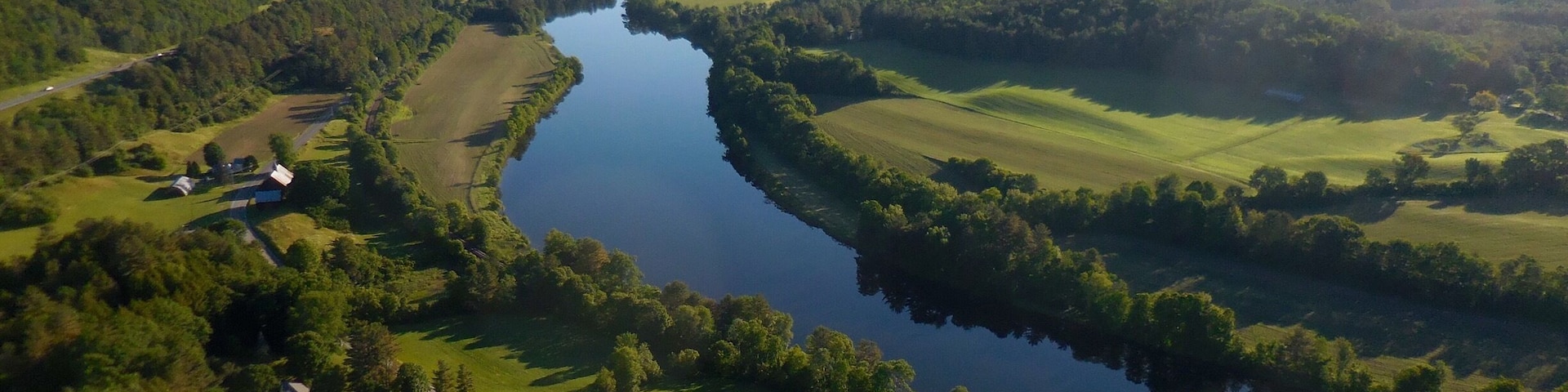 A 6:15 a.m. departure from Post Mills Airport, VT in your hot air balloon gets this spectacular view of Vermont to the left of the river, and New Hampshire to the right. This perspective is looking essentially northwards. Farm lands and forest nestled along what was in colonial times a mighty river of commerce and transportation. When Vermont separated from NH, and to protect those assets, NH insisted the border between NH and VT would be the high water mark on the westerly side of the river.