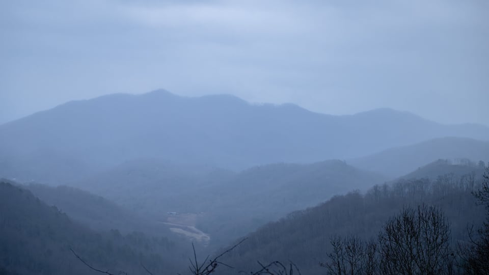 A misty mountain landscape with rolling hills and a valley.