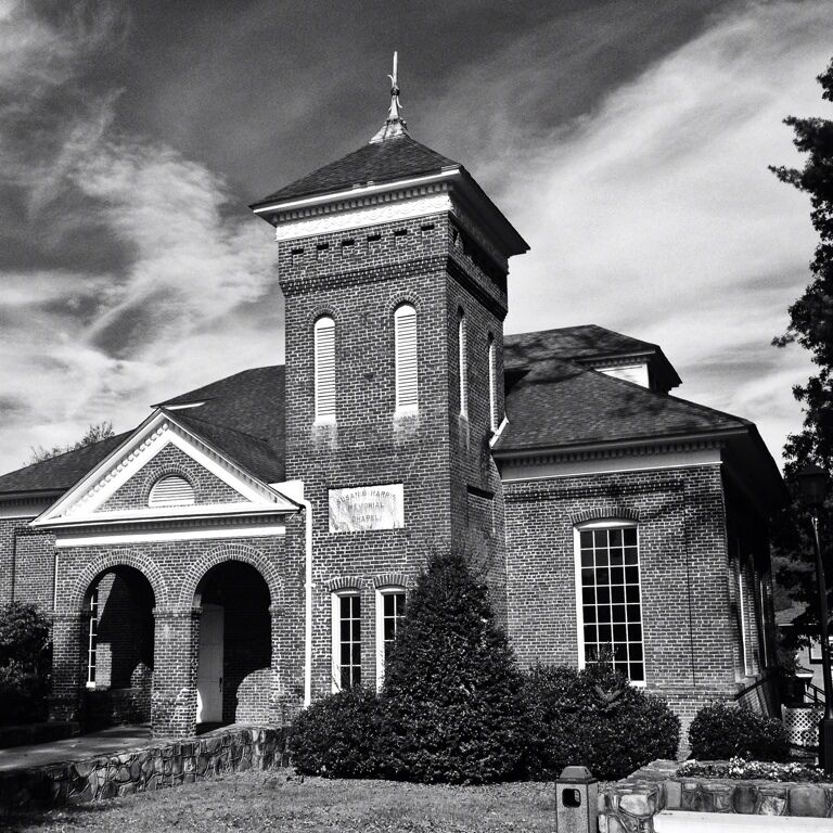 A historic brick building with a central tower, arched entrance, and a signboard.
