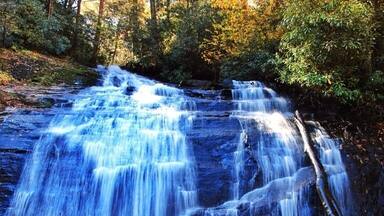 Uma cascata despencando sobre um penhasco rochoso, cercada por árvores.