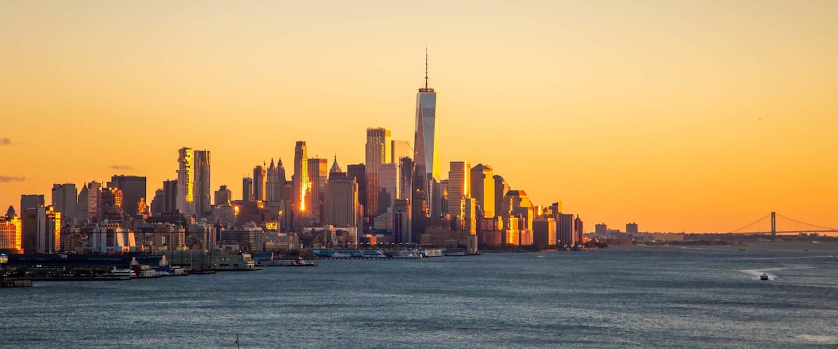A city skyline at sunset with a prominent skyscraper in the center.