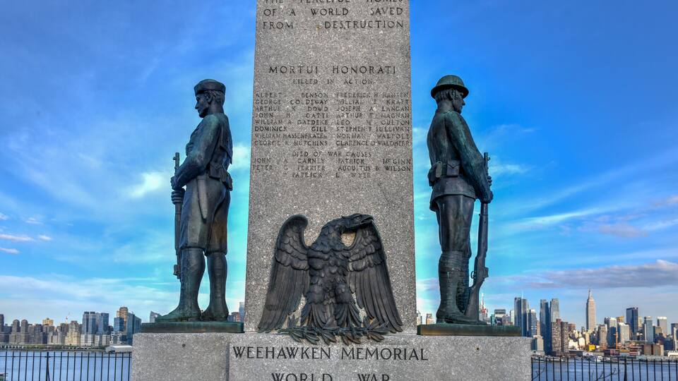 A memorial with two statues and an eagle emblem, with a city skyline in the background.