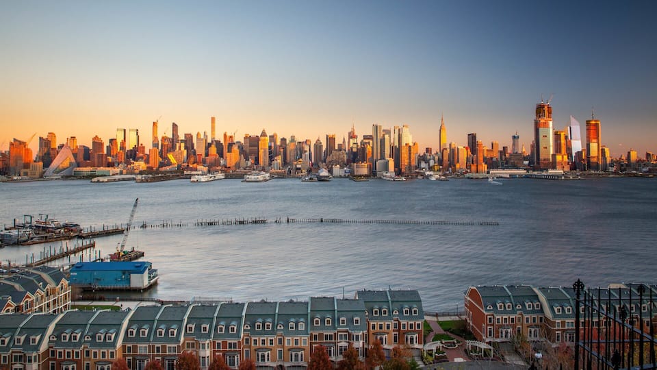 A city skyline at sunset with a river in the foreground.
