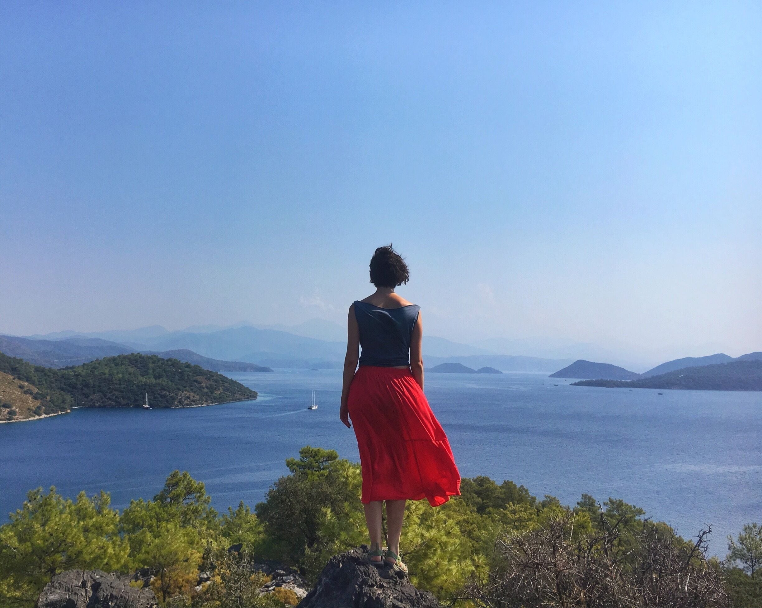 Una mujer de pie sobre un saliente rocoso con vistas a una gran extensión de agua, islas lejanas y montañas.