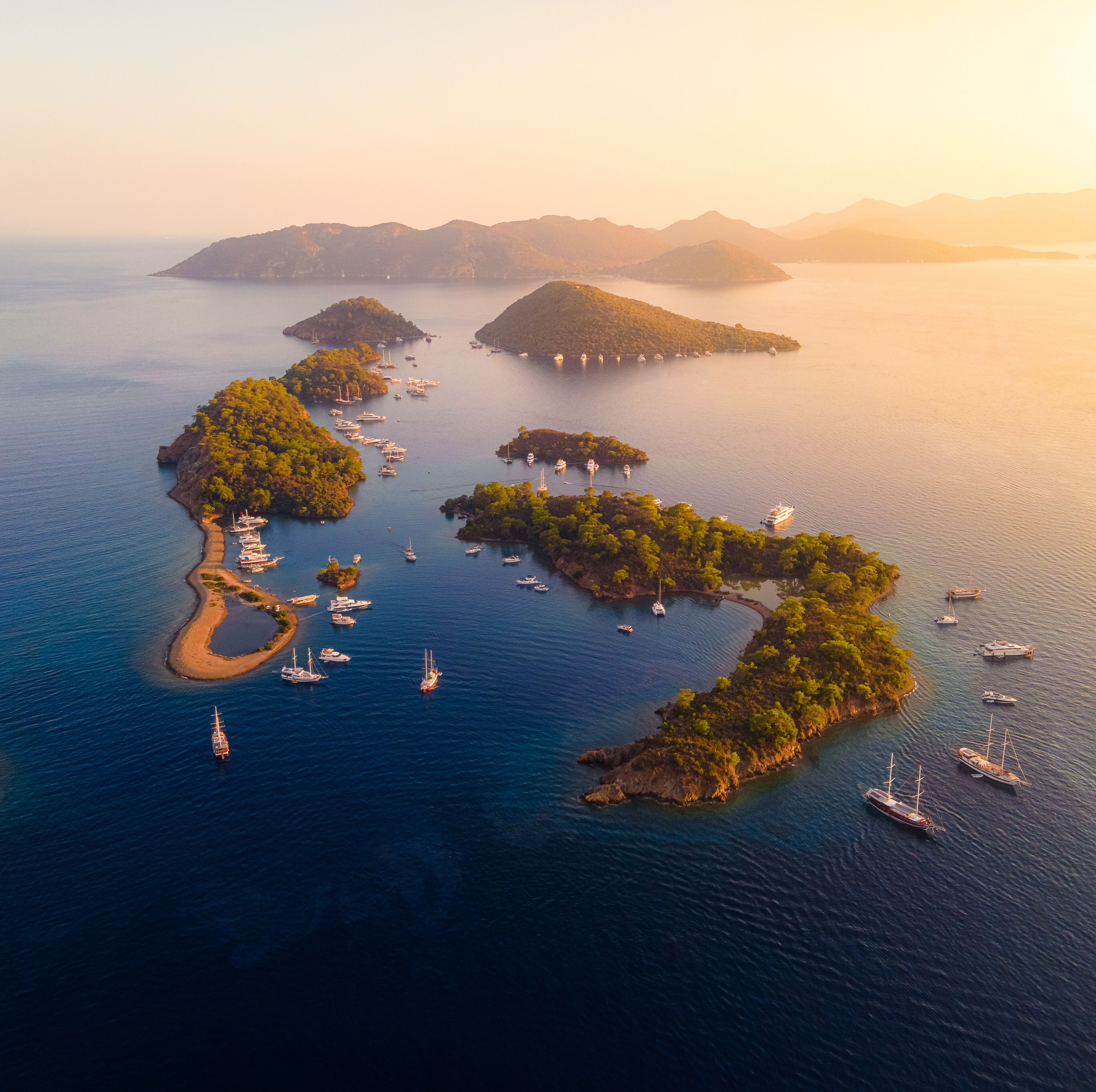 An aerial view of a coastal area with multiple islands, clear blue waters, and numerous boats anchored around the islands.