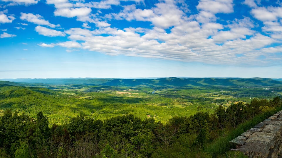A panoramic view of a lush green valley with rolling hills and a stone wall in the foreground.