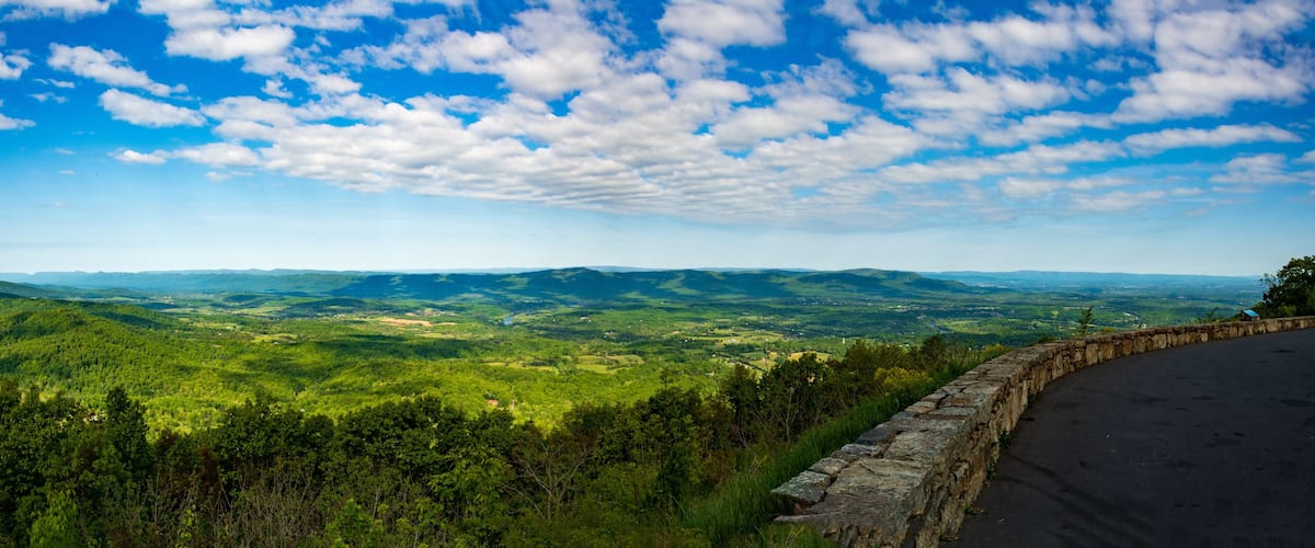 A panoramic view of a lush green valley with rolling hills and a stone wall in the foreground.