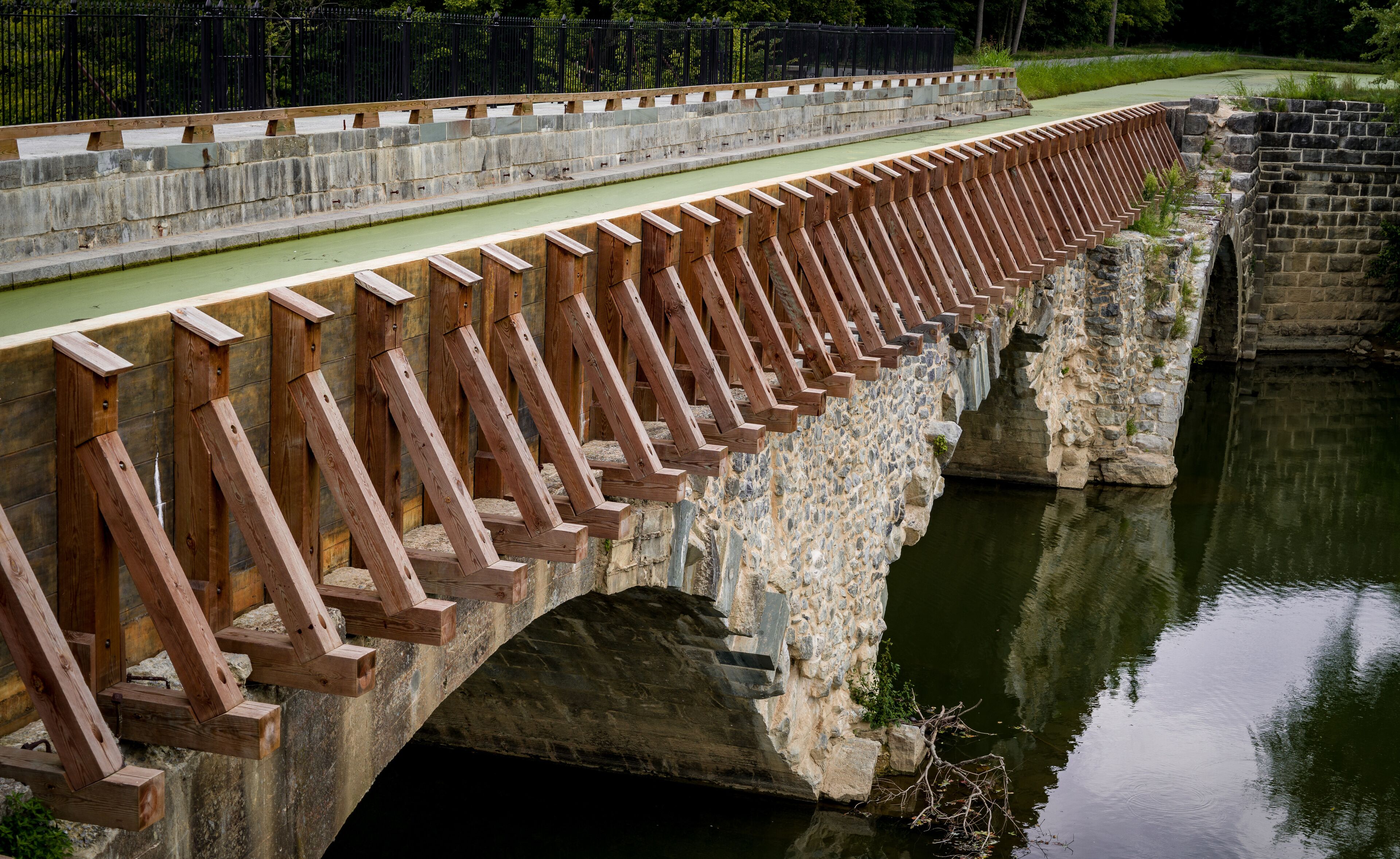 A stone bridge with wooden railings over a calm river.