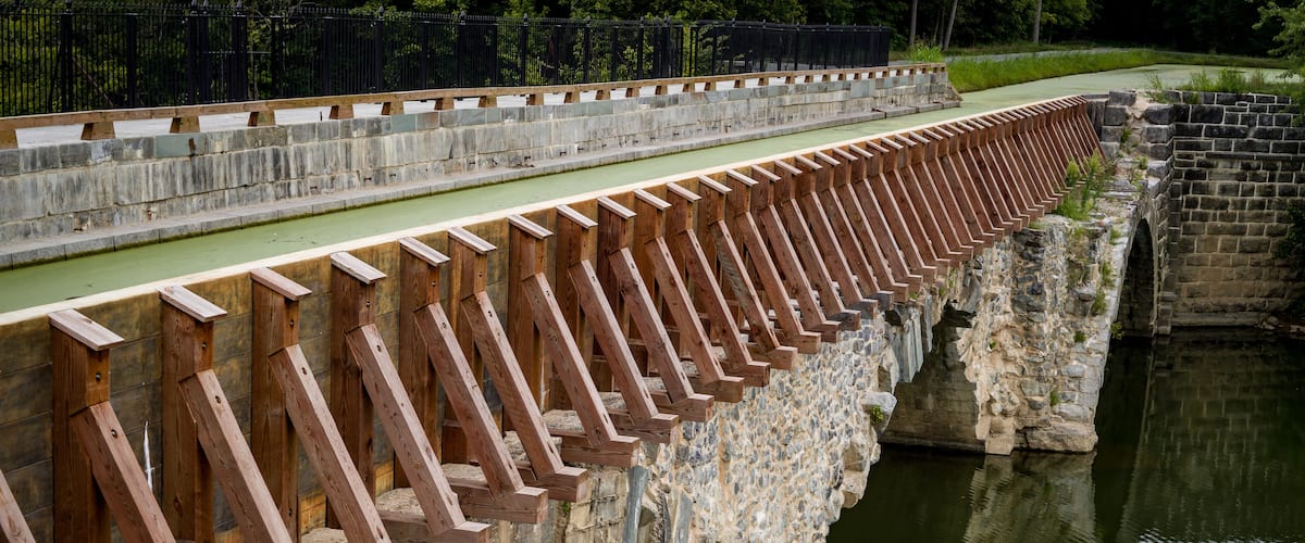 A stone bridge with wooden railings over a calm river.