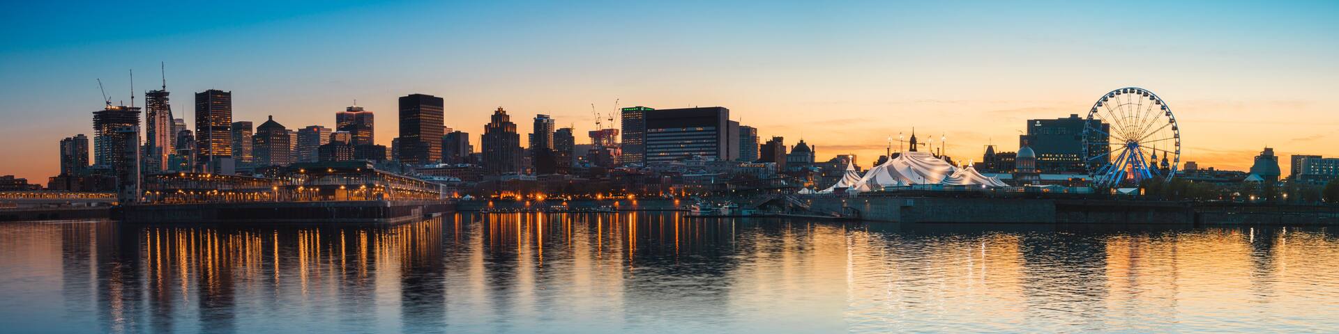 A city skyline at dusk with a prominent Ferris wheel and a waterfront reflecting the buildings.