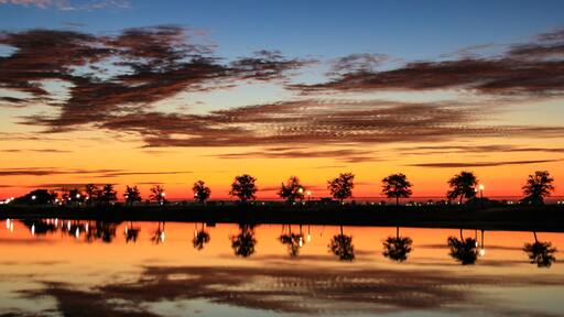 A sunset over a calm body of water with trees silhouetted against the sky.