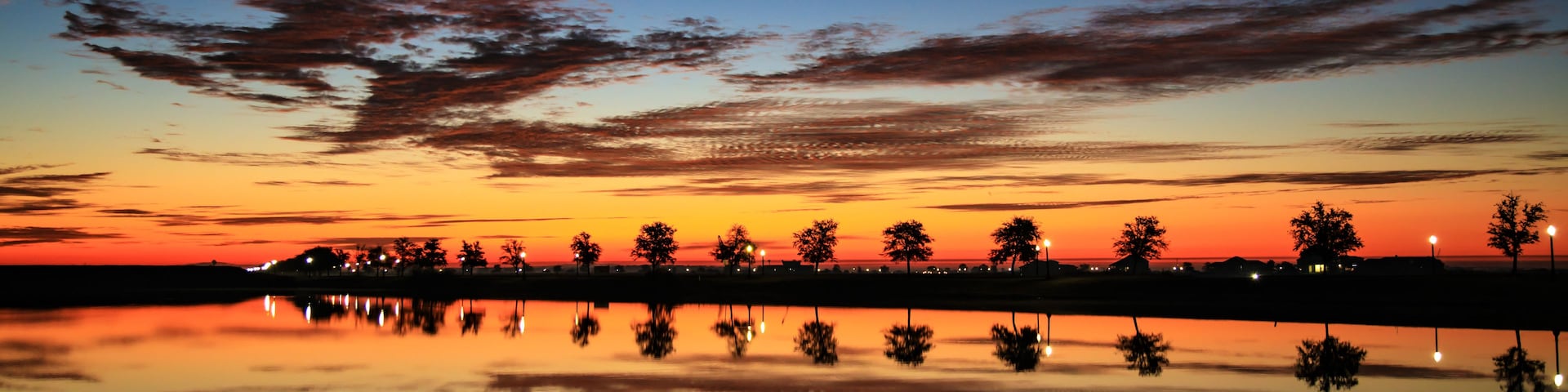 A sunset over a calm body of water with trees silhouetted against the sky.