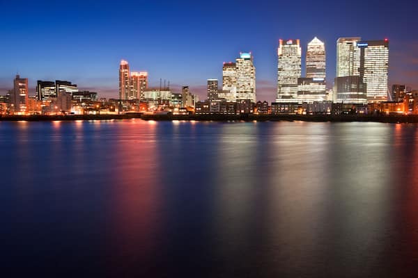 Une vue sur les gratte-ciel d’une ville au crépuscule, les bâtiments illuminés se reflétant sur l’eau.