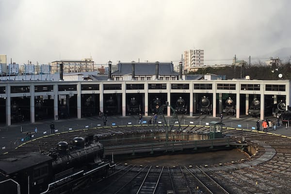 Une gare avec de nombreuses voies et un grand bâtiment dont les portes sont numérotées.
